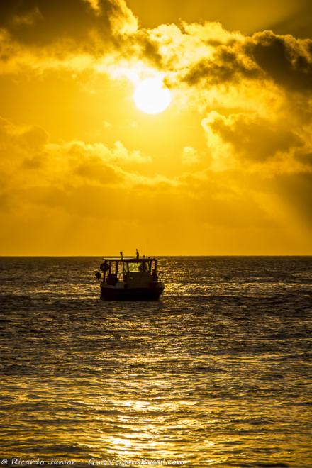 Imagem do céu alaranjado e um barco charmoso na Praia da Conceição.